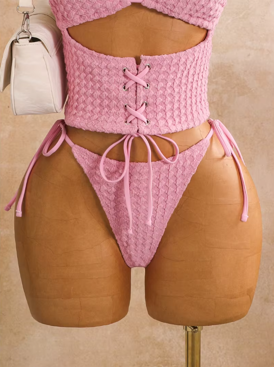 Close-up of pink textured bikini set with lace-up waist panel, metal eyelets and tie-side high-leg bottoms.