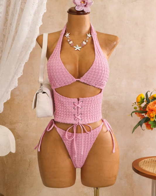 Pink textured halter bikini set displayed on mannequin with lace-up waist panel and tie-side bottoms.