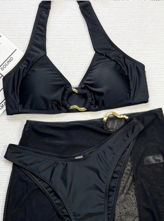 Close-up of black bikini and sheer sarong set with gold-tone ring hardware and smooth swim fabric.