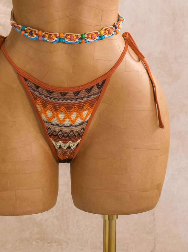 Close-up of saffron orange textured tie-side bikini bottoms with bronze zigzag pattern and warm contrast binding.