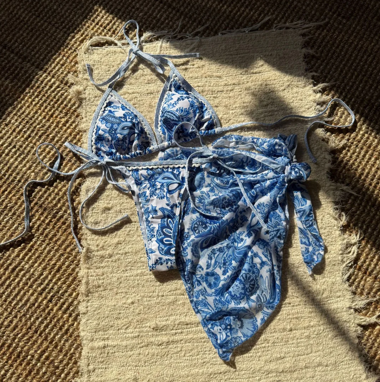 Santorini blue and white bikini and matching sarong set flat lay on a woven rug.