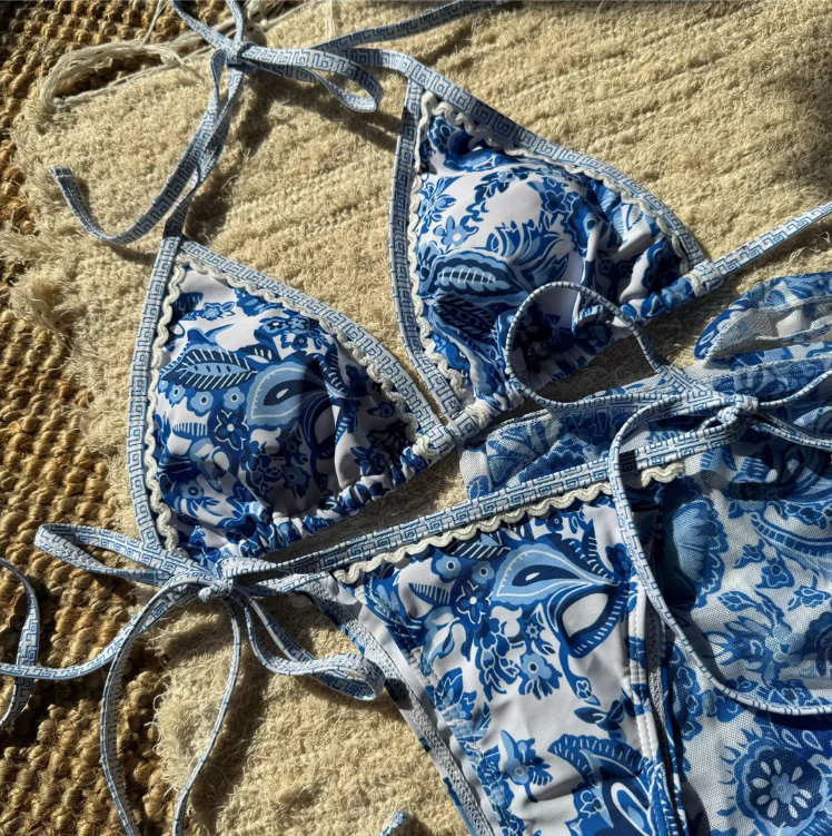 Close-up of blue and white paisley floral triangle bikini with decorative trim and matching sarong.