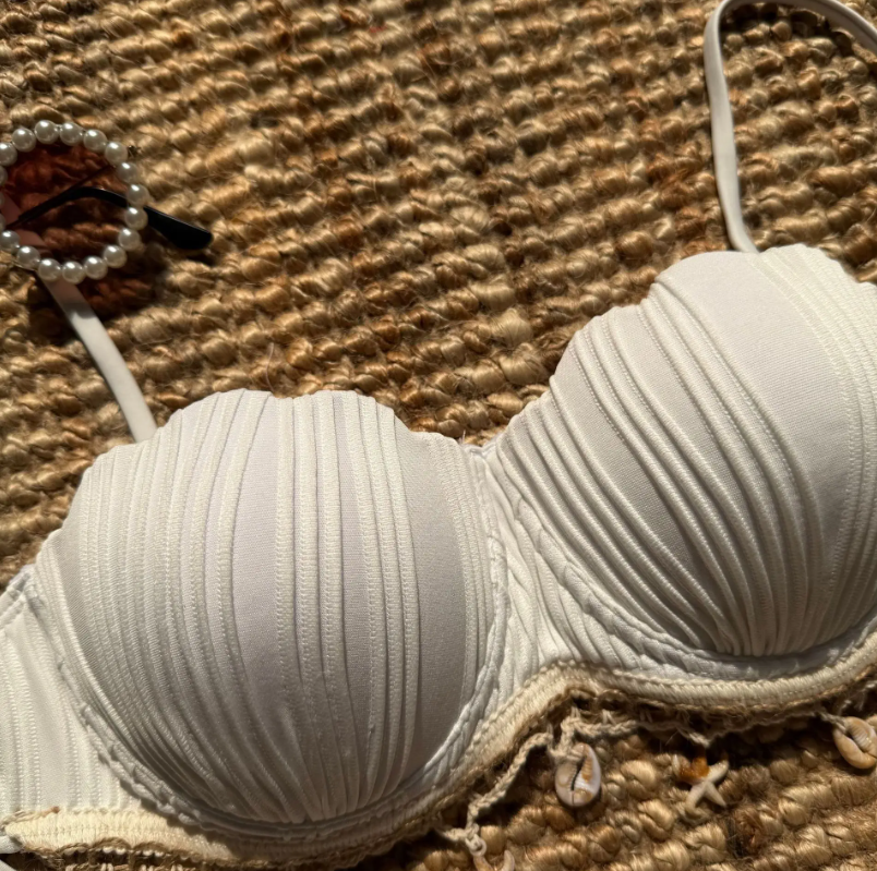 Close-up of ivory pleated bikini top with underbust trim, shell charm detailing and structured cup shape.