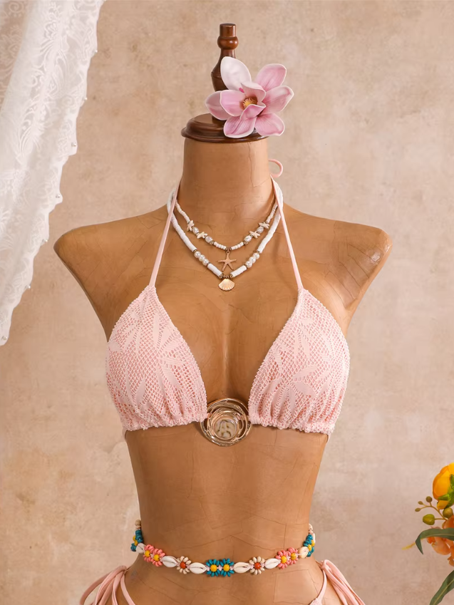 Close-up of camellia blush openwork triangle bikini top with botanical texture, halter ties and sculptural gold-tone hardware.