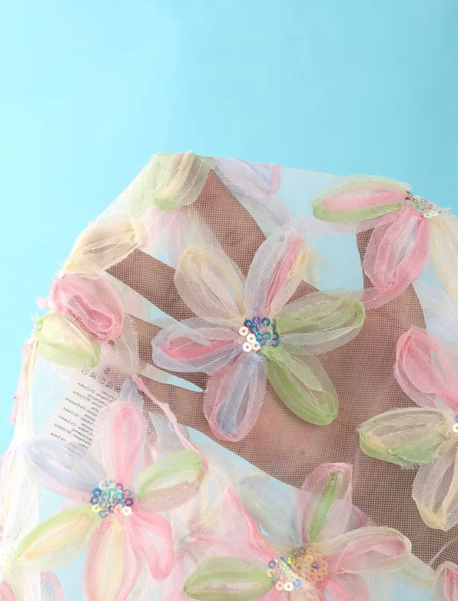 Close-up of pink sheer mesh fabric with pastel dimensional floral appliqué and sequin-centred petal detailing.