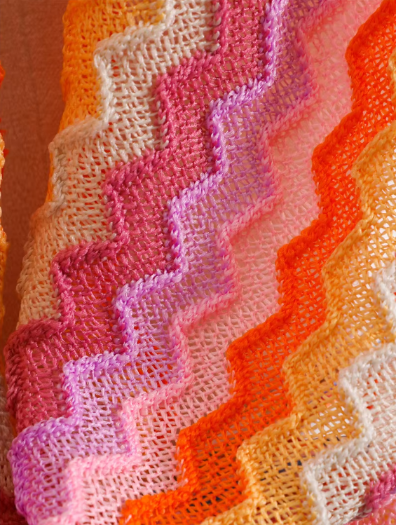 Close-up of flamingo open-knit chevron fabric in pink, orange, cream and lilac tones.