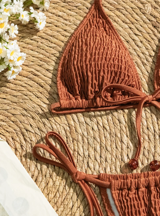 Close-up of terracotta smocked bikini fabric with triangle cup, tie straps and bead-finished detailing.