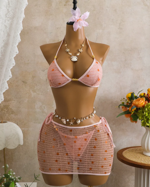 Pink crochet-look bikini and sheer mini skirt set displayed on mannequin with sequin embellishment and gold-tone bead accents.