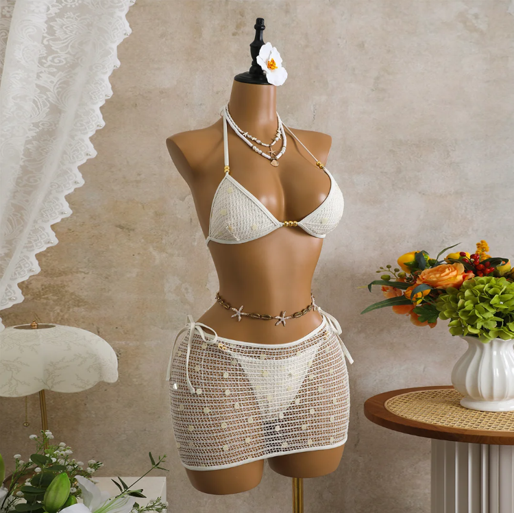 Angled front view of white crochet-look bikini and matching sheer mini skirt with reflective sequin detailing.