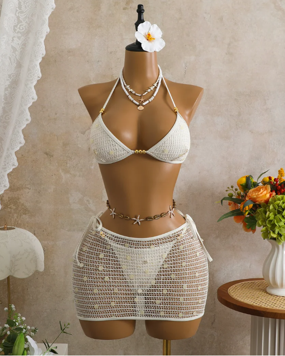 White crochet-look bikini and sheer mini skirt set displayed on mannequin with sequin embellishment and gold-tone bead accents.