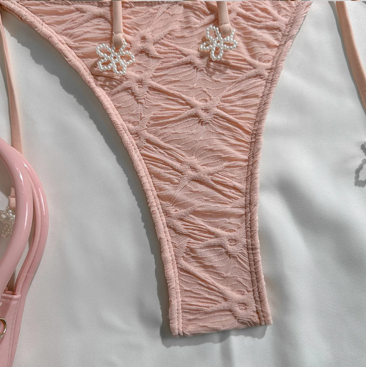 Close-up of Valencia bikini bottoms showing blush textured fabric and floral charm detail on the side ties.