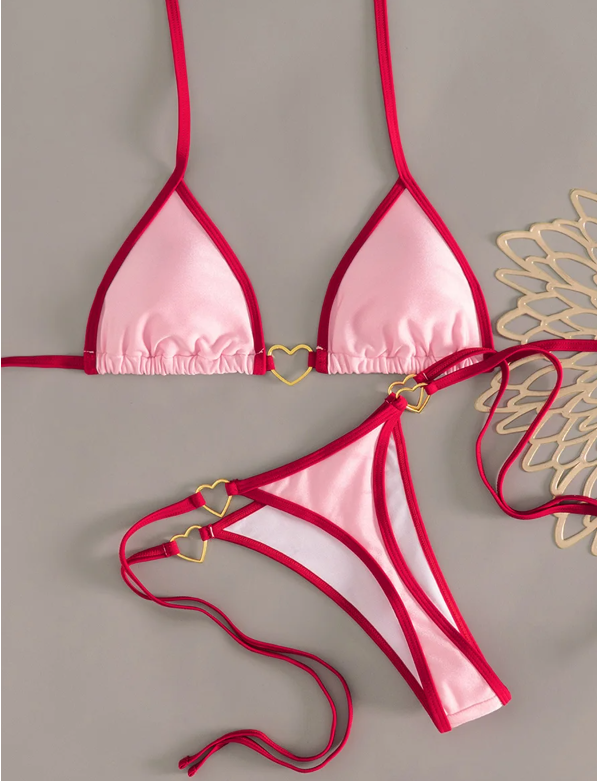 Flat lay of the Valentina bikini set in pink with red trim, featuring a triangle halter top and tie-side bikini bottoms with gold heart hardware.