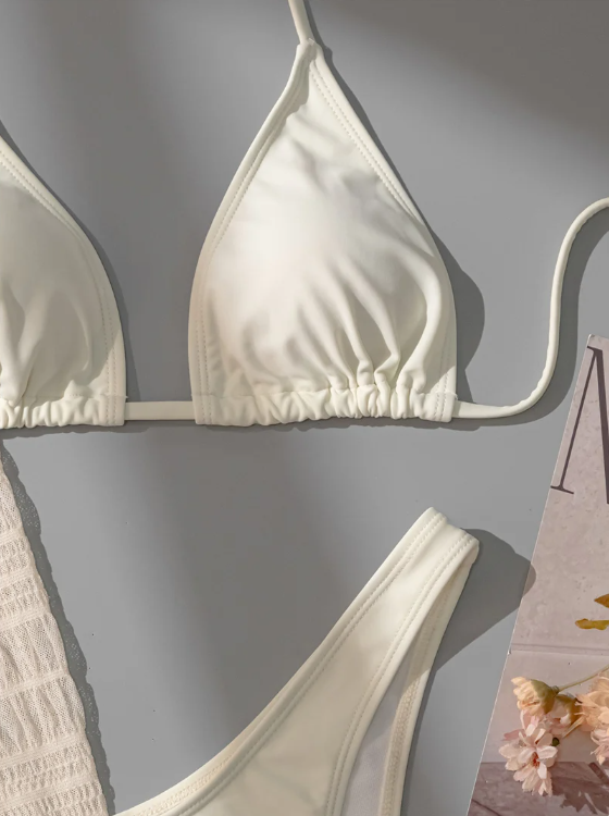 Close-up flat lay of ivory bikini top and bottom styled with the Venice Dress cover-up.